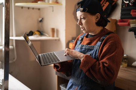 Woman in workwear using laptop working in garage or repair shop. small business