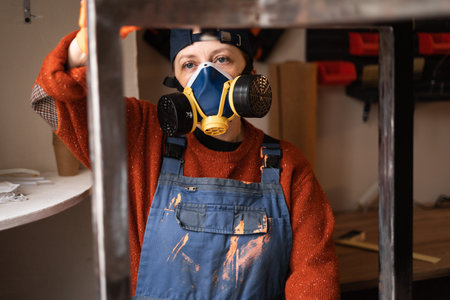 Portrait woman skilled laborer wearing respirator painting steel table frame using brush technique