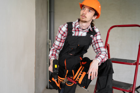 Pensive male laborer, builder or repairman ready for repairing or building, wears overalls, tool...