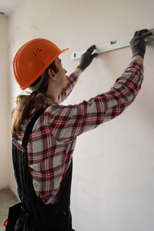 Contractor, handyman, builder in uniform measuring wall using bubble spirit level. home renovation...