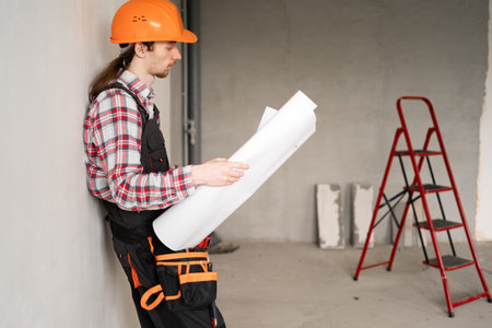 Male Construction worker wear hard hat reading blueprints inspecting building site