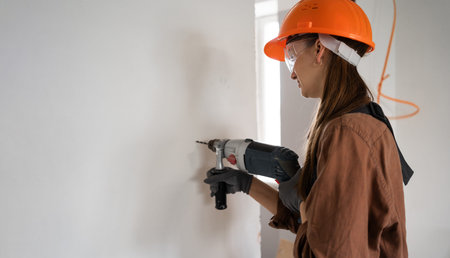 Female construction worker using hammer drill. Builder woman with hammer drill making hole in wall