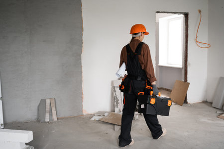 Woman handyman with toolbox walk go in unfinished building. Instruments for renovation apartment...