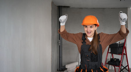 Woman Builder. Happy success female Architect in work overalls and hardhat celebrating win or victory in unfinished building. repair, construction and building concept. banner.の写真素材