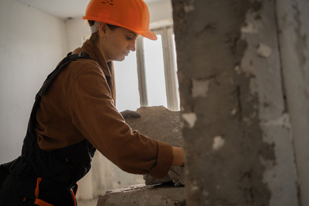 Female builder in hardhat lifting heavy concrete slabs