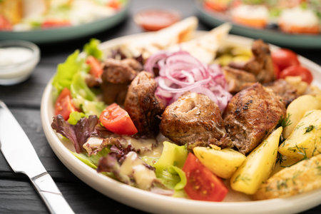 Flat lay of grilled meat shish kebab with roasted potatoes and fresh vegetables on plateの写真素材