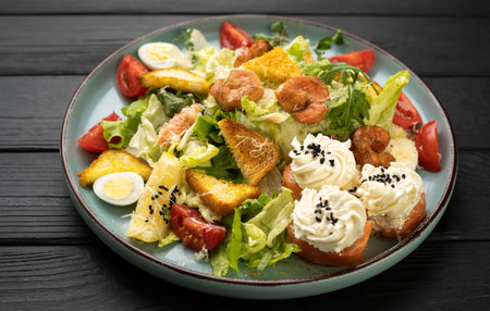 Fresh caesar salad with fried shrimps cherry tomatoes quail eggs and crunchy croutons on plateの写真素材