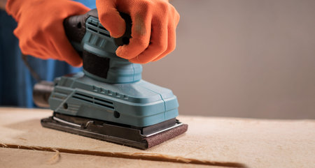 Close up of a carpenter using a sheet sander for wood surface finishing. Professional woodworking...