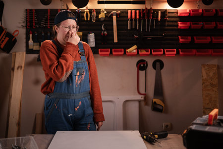 Woman joiner wears workwear in workshop scene with tools hanging on wall cover nose. female...
