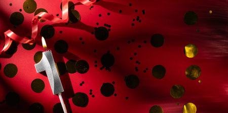 Concept of celebrating birthday and anniversary. Number 1 one silver celebration birthday candle on festive red background with large golden confetti. One year birthday.の写真素材