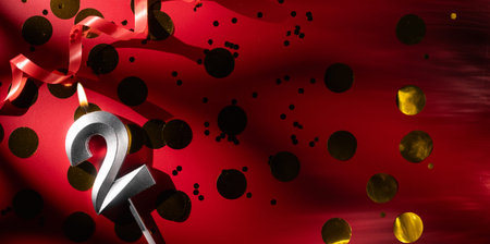 Concept of celebrating birthday and anniversary. Number 2 two silver celebration birthday candle on festive red background with large golden confetti. Two years birthday.の写真素材
