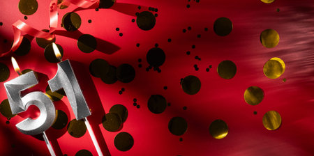 Concept of celebrating birthday and anniversary. Number 51 fifty-one silver celebration birthday candle on festive red background with large golden confetti. Fifty-one years birthday.の写真素材
