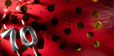 Concept of celebrating birthday and anniversary. Number 70 seventy silver celebration birthday candle on festive red background with large golden confetti. Seventy years birthday.の写真素材