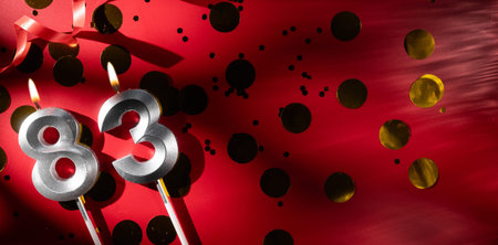 Concept of celebrating birthday and anniversary. Number 83 eighty-three silver celebration birthday candle on festive red background with large golden confetti. Eighty-three years birthday. flat layの写真素材