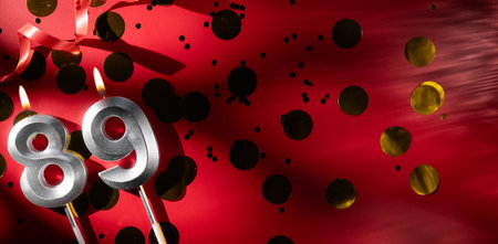 Concept of celebrating birthday and anniversary. Number 89 eighty-nine silver celebration birthday candle on festive red background with large golden confetti. Eighty-nine years birthday. flat layの写真素材