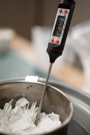 measuring soy wax temperature with a thermometer during candle making