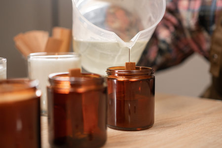 Concept of creative hobby and handmade candles. female hands pouring melted soy wax into jar.の写真素材