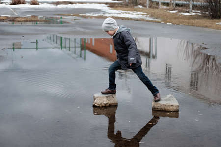Preschool boy jumping over the puddles on the rocksの写真素材