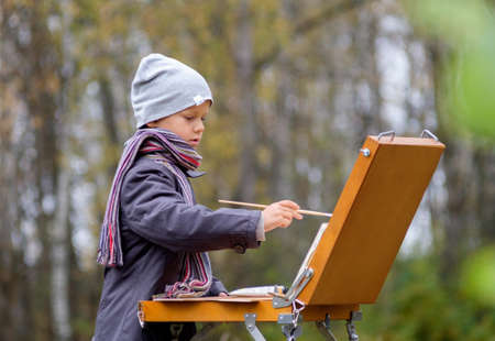 Young painter with an easel in the autumn forest paints a picture from natureの写真素材