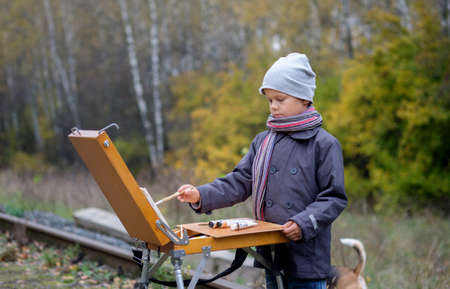 Young painter with an easel in the autumn forest paints a picture from natureの写真素材