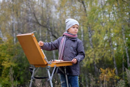 Young painter with an easel in the autumn forest paints a picture from natureの写真素材