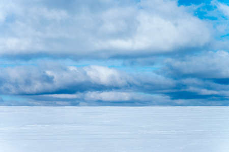 Winter background landscape with a view of snow-covered fields and blue sky with white cloudsの写真素材