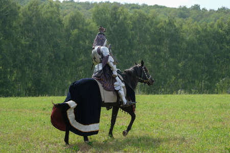 Medieval knight in metal armor on a horse in a fieldの写真素材