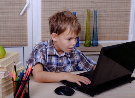 European boy of primary school age performs educational work at the table with laptop and books