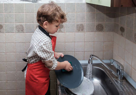 boy European appearance of the house washes the dishes in the sinkの写真素材