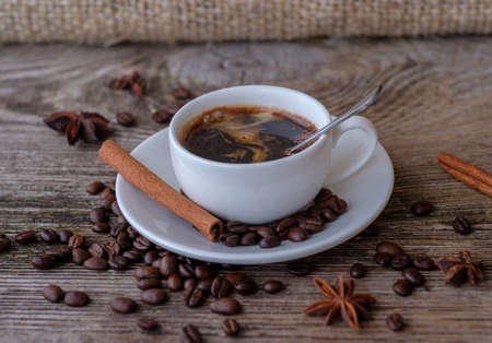 black coffee in a white Cup on a wooden table with coffee beans , cinnamon and aniseの写真素材