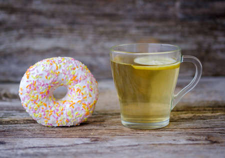 green tea with lemon in a glass Cup and round donuts with colorful glaze on a wooden tableの写真素材