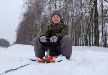 European boy happily rides through the snow on a sled in winter day for a walkの写真素材