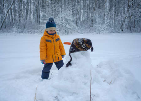 Cute European boy and snowman in winter snowy forestの写真素材