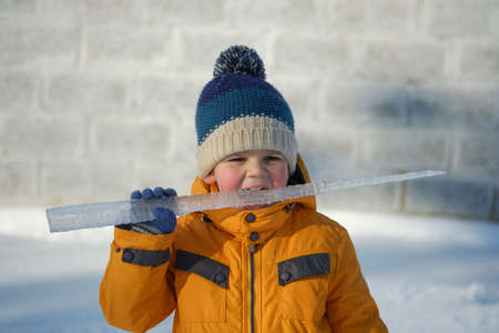 Cute European boy with big icicle on a walk on a Sunny winter dayの写真素材