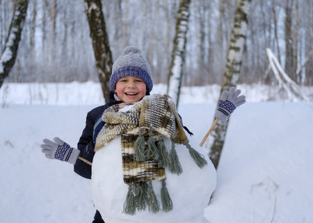 cute European boy and the funny snowman in the snowy woods on a winter day in the snow