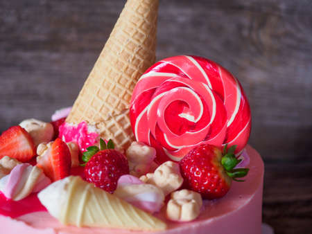 Beautiful soft pink cake homemade cakes with strawberries, waffle cone and a round Lollipop on a wooden tableの写真素材
