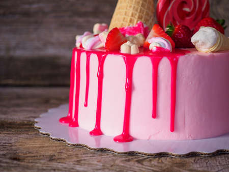 Beautiful soft pink cake homemade cakes with strawberries, waffle cone and a round Lollipop on a wooden tableの写真素材