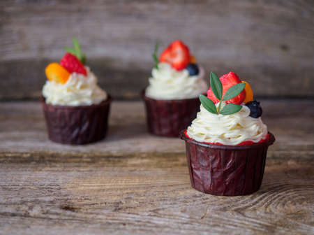 Beautiful cupcake with curd cream, strawberries and green leaf on a wooden tableの写真素材