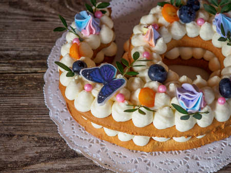 Beautiful homemade cake in the form of six figures with berries and curd cream on a wooden tableの写真素材