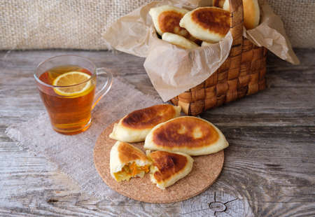 homemade sauerkraut pies on a wooden table, a basket of pies and lemon teaの写真素材