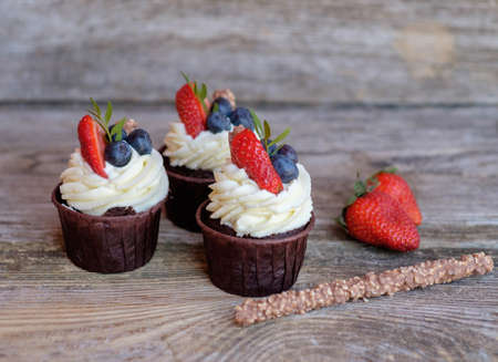 chocolate cupcake with cheese cream, strawberries, blueberries on wooden tableの写真素材