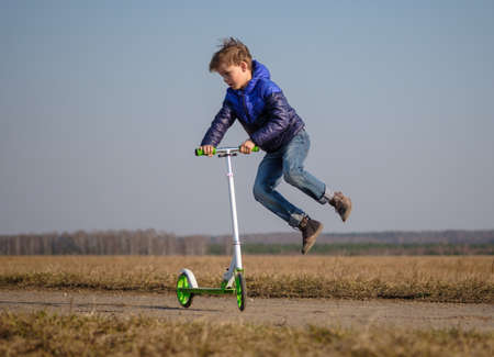 cute European boy riding and doing tricks on scooter while walkingの写真素材