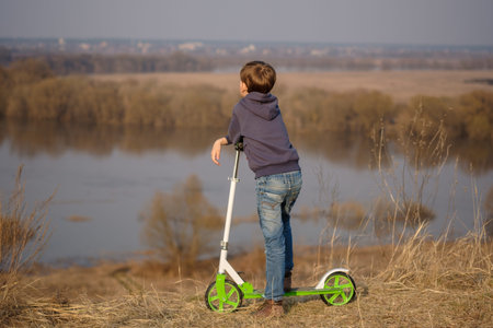 European boy with a scooter on the high Bank of the river during the spring flood