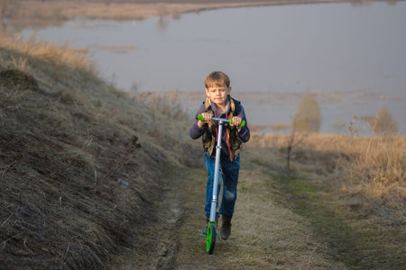 European boy with a scooter on the high Bank of the river during the spring floodの写真素材