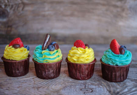 multicolored cupcakes with cheese cream and strawberries on a wooden tableの写真素材