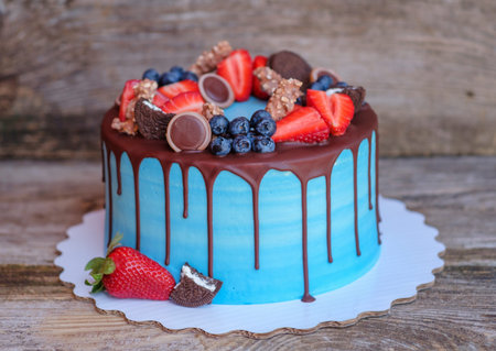 beautiful homemade cake with blue cream and chocolate glaze, decorated with strawberries and...