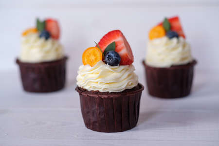 beautiful homemade cupcakes with white cheese cream, strawberries and blueberries on white tableの写真素材