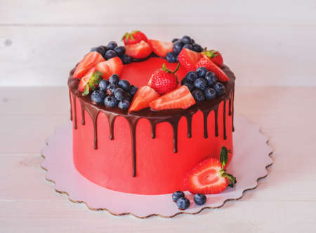Beautiful home made bright red cake with strawberry and blueberry berries, chocolate frosting on white tableの写真素材