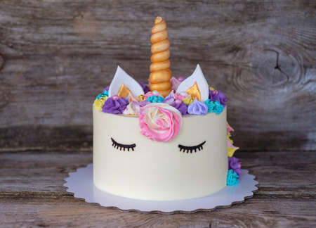 beautiful homemade cake in the form of a unicorn with cream colored flowers on a wooden tableの写真素材