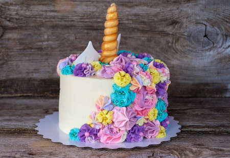 beautiful homemade cake in the form of a unicorn with cream colored flowers on a wooden tableの写真素材